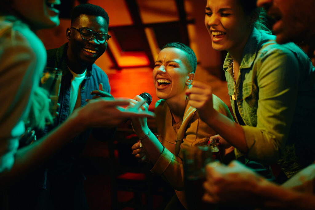 Group of happy friends singing karaoke during a night party at the pub.